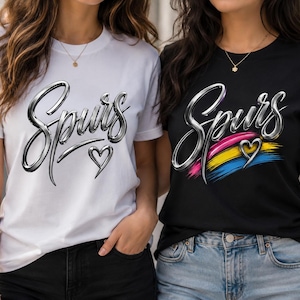 May include: A white t-shirt and a black t-shirt, each featuring the word Spurs in a metallic silver script font. The white shirt includes a small silver heart outline, while the black shirt features a colorful brushstroke design and a heart.