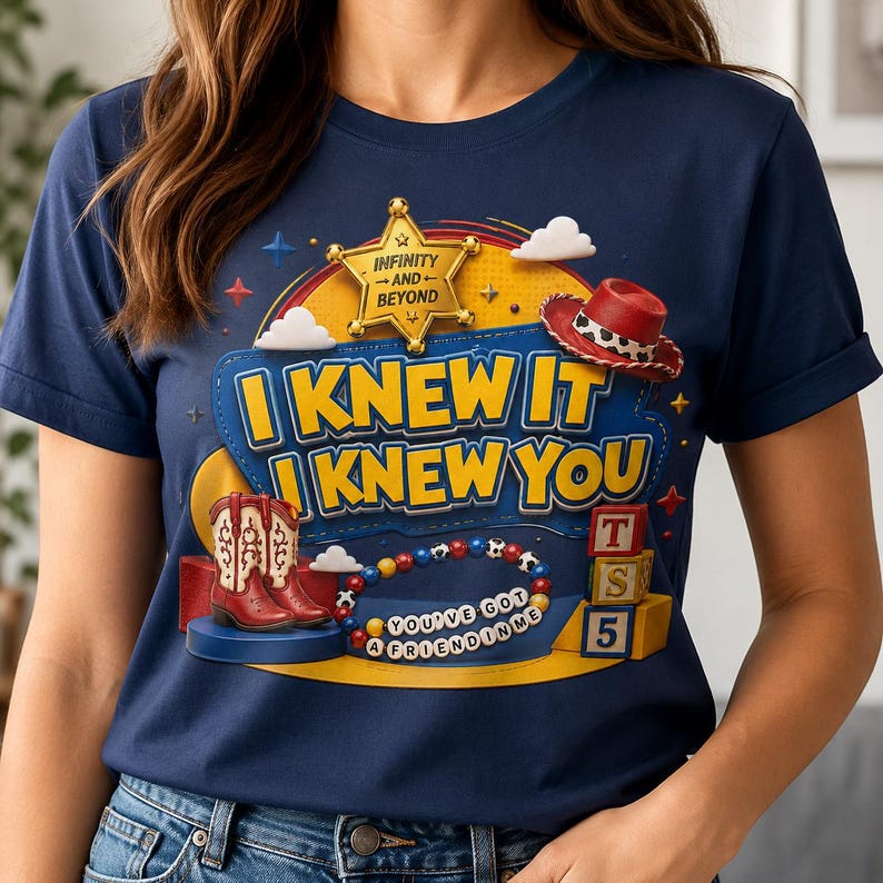 Pode incluir: Uma t-shirt azul-marinho com uma estampa gr&aacute;fica contendo o texto "I KNEW IT I KNEW YOU" e "YOU'VE GOT A FRIEND IN ME". O design inclui uma estrela de xerife dourada, um chap&eacute;u de cowboy vermelho, botas vermelhas e brancas, uma pulseira de contas coloridas e blocos de brinquedo.