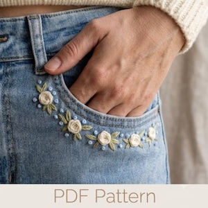May include: Light blue denim jeans featuring an embroidered floral design along the edge of the front pocket. The embroidery consists of small white roses with green leaves and light blue French knot accents. The text PDF Pattern is visible.