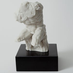 May include: A white sculpture of a torso, mounted on a black rectangular base. The sculpture has a rough, textured surface and depicts the upper body of a human figure. The base provides a contrasting dark element to the sculpture.