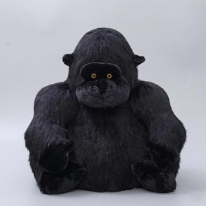 May include: A plush gorilla toy with black fur, a dark face, and small, golden eyes. The gorilla has large arms and feet, and is sitting upright. The toy is designed to resemble a gorilla.