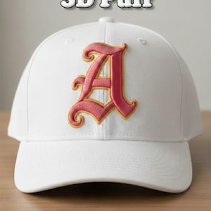 Puede incluir: Gorra de béisbol blanca con visera curva, con una letra "A" rosa bordada con ribetes dorados. El texto "3D Puff" está encima de la gorra. Debajo de la gorra está el texto "DST PES JEF EXP VP3 HUS".