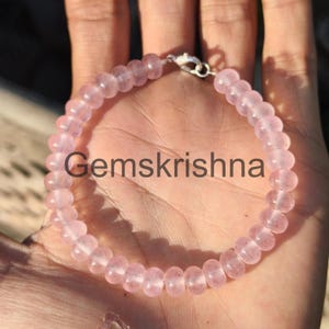 Könnte beinhalten: Ein hellrosa Perlenarmband mit einem silbernen Verschluss. Das Armband besteht aus runden, durchscheinenden Perlen. Der Text "Gemskrishna" ist auf dem Bild aufgedruckt.