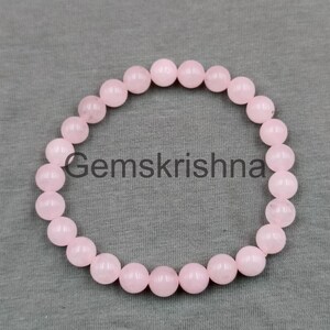 Könnte beinhalten: Ein Armband aus Rosenquarz-Perlen. Das Armband besteht aus hellrosa, runden Perlen. Der Text "Gemskrishna" ist in der Mitte des Armbands aufgedruckt.