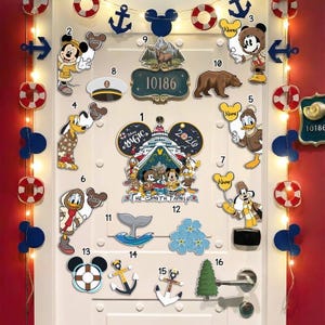 May include: A white door decorated with Disney-themed cutouts, including Mickey Mouse, Donald Duck, and Pluto. Decorative anchors, life preservers, and a door sign with the number 10186 are also present. The door handle is silver.