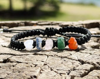 May include: A black braided cord bracelet featuring five raw, irregularly shaped stones in white, blue, pale pink, green, and orange. The bracelet has a woven texture and adjustable cord ends, showcasing a variety of natural mineral colors.
