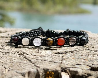 May include: A black cord bracelet featuring seven round, polished gemstone beads in various colors including dark red, white, translucent, brown, orange, grey, and black, arranged in a row and secured with a woven macrame knot closure.
