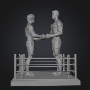 May include: A gray sculpture of two boxers shaking hands in a boxing ring. The boxers are muscular and wearing boxing gloves and shorts. The ring has ropes and posts, and the base is rectangular.