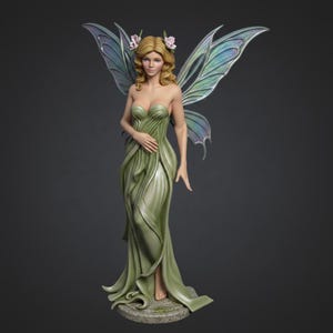 May include: A detailed figurine of a fairy with blonde hair, wearing a flowing green dress. The fairy has iridescent wings and is adorned with pink flowers in her hair. The statue is standing on a stone base.