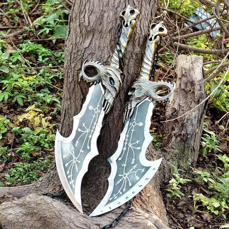 May include: Two decorative swords with silver-coloured blades and ornate handles. The handles feature a skull design, and the blades have intricate patterns. The swords are leaning against a tree trunk, with a chain visible.