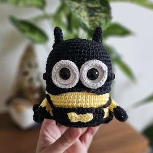 Op de afbeelding: Een handgemaakt gehaakt bijenspeeltje. De bij is zwart en geel met grote, ronde ogen met witte randen. Het heeft kleine antennes en een gebogen lichaam. Het speelgoed wordt in een hand gehouden.