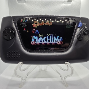 Könnte beinhalten: Schwarze Sega Game Gear-Handheld-Konsole, die einen farbenfrohen Spielbildschirm mit dem Text "Dr. Robotnik's Mean Bean Machine" anzeigt. Die Konsole hat einen Lautsprecher, ein Steuerkreuz und eine Starttaste.
