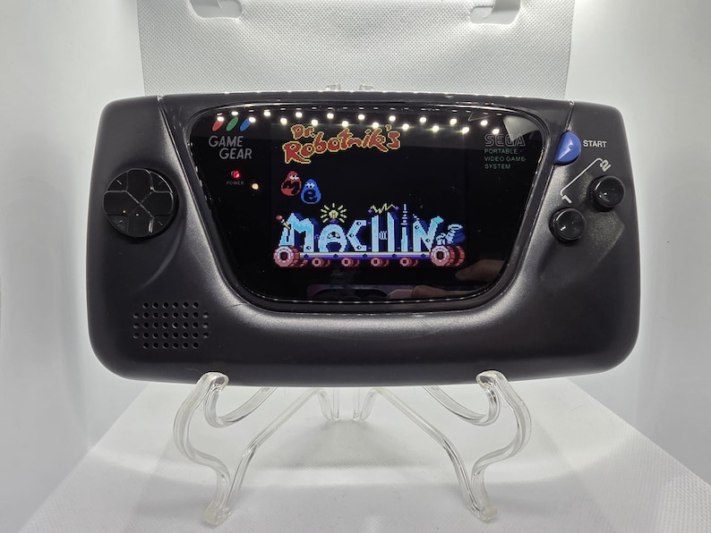 K&ouml;nnte beinhalten: Schwarze Sega Game Gear-Handheld-Konsole, die einen farbenfrohen Spielbildschirm mit dem Text "Dr. Robotnik's Mean Bean Machine" anzeigt. Die Konsole hat einen Lautsprecher, ein Steuerkreuz und eine Starttaste.