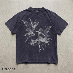 May include: A graphite-colored short-sleeve t-shirt featuring a detailed white graphic print of two winged figures dancing amidst a field of small stars. The shirt has a crew neckline and a faded, worn-in appearance with visible texture.
