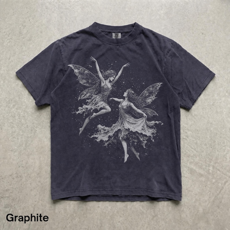 May include: A graphite-colored short-sleeve t-shirt featuring a detailed white graphic print of two winged figures dancing amidst a field of small stars. The shirt has a crew neckline and a faded, worn-in appearance with visible texture.