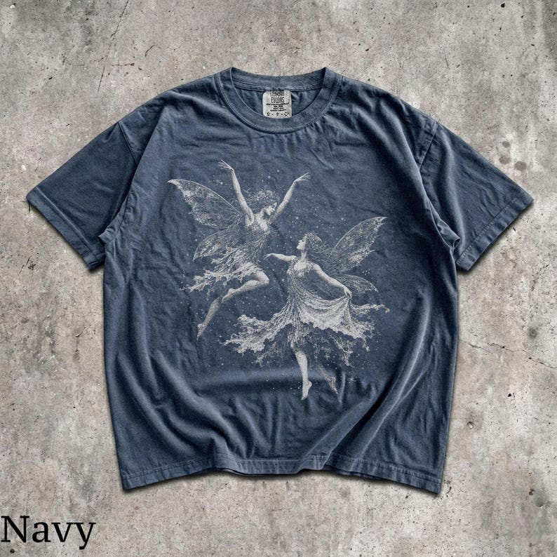 May include: A navy blue short-sleeve t-shirt featuring a white graphic print of two winged figures dancing. The shirt has a crew neckline and a visible brand tag at the inner collar. The fabric has a washed, faded appearance throughout.