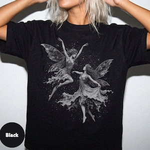 May include: A black short-sleeve t-shirt featuring a detailed white graphic print of two winged fairies dancing amidst a field of stars. The design depicts the figures with flowing garments and intricate wings, centered on the chest area.