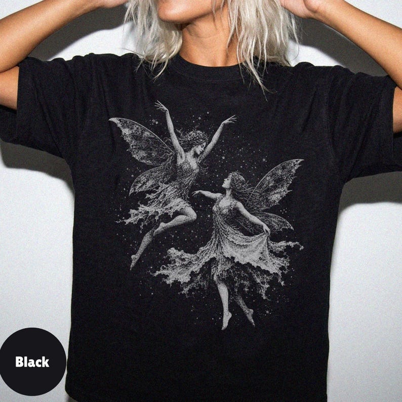 May include: A black short-sleeve t-shirt featuring a detailed white graphic print of two winged fairies dancing amidst a field of stars. The design depicts the figures with flowing garments and intricate wings, centered on the chest area.