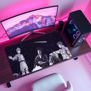 Puede incluir: Alfombrilla de escritorio rectangular negra con una ilustración estilo manga de tres figuras sobre un fondo estrellado. La alfombrilla está colocada sobre un escritorio de madera, con un monitor de ordenador, una torre de PC y otros accesorios visibles.