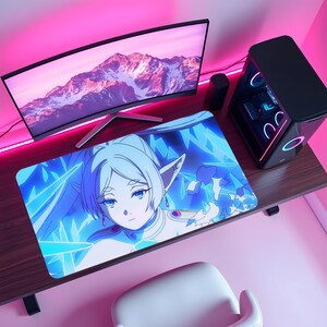 Puede incluir: Alfombrilla de ratón rectangular azul y blanca de estilo anime con un personaje femenino de pelo largo azul claro y ojos azules. La alfombrilla está sobre un escritorio de madera con un monitor de ordenador, una torre de ordenador y una silla blanca.