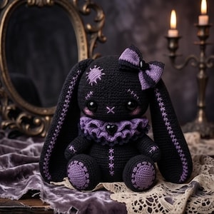 Pode incluir: Um coelho de pelúcia de crochê preto com orelhas longas com costuras roxas, uma gola de babados roxa com um pingente de coração preto, um laço roxo em uma orelha e remendos circulares roxos nos pés. O coelho tem olhos pretos grandes.