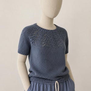 May include: A short-sleeved, blue knit top with a decorative openwork yoke. The top is paired with blue drawstring pants. The outfit is displayed on a mannequin.