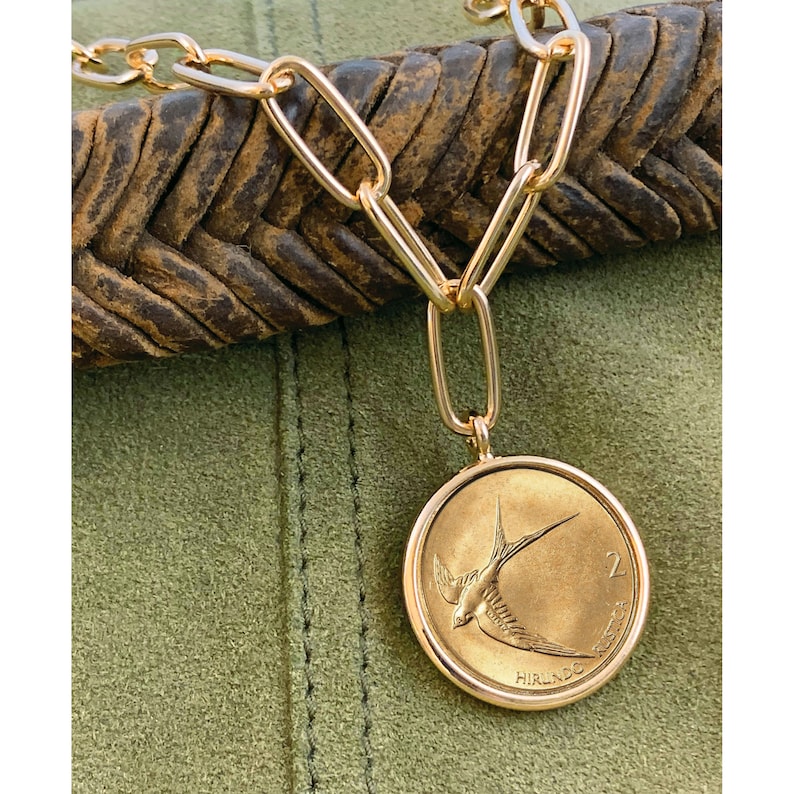 K&ouml;nnte beinhalten: Goldkette mit einem goldenen M&uuml;nzenanh&auml;nger, der ein stilisiertes Vogelmotiv und den Text "2 IRISH POUNDS" zeigt.