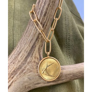 K&ouml;nnte beinhalten: Eine goldene Kettenkette mit einem gro&szlig;en, runden Anh&auml;nger, der eine goldene M&uuml;nze mit einem Vogelmotiv zeigt. Die M&uuml;nze tr&auml;gt den Text "2 PENCE" und "EIRE".