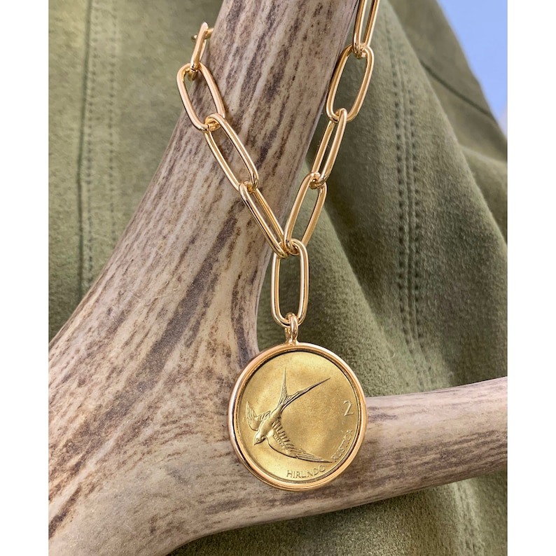 K&ouml;nnte beinhalten: Eine goldene Kettenkette mit einem gro&szlig;en, runden Anh&auml;nger, der eine goldene M&uuml;nze mit einem Vogelmotiv zeigt. Die M&uuml;nze tr&auml;gt den Text "2 PENCE" und "EIRE".