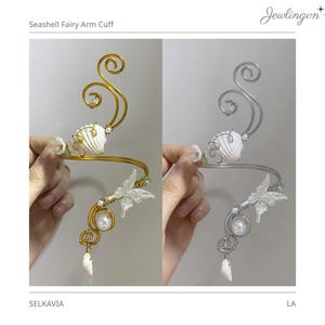 May include: A gold-toned and silver-toned arm cuff with seashell and butterfly accents. The cuff features a seashell, pearl, and butterfly design. The arm cuff is a unique piece of jewelry.