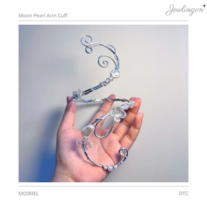 May include: A silver-toned wire arm cuff featuring a spiral design adorned with small white pearls and clear, flower-shaped beads. The structure includes delicate swirls and wire-wrapped accents, creating an open, flexible band for the upper arm.