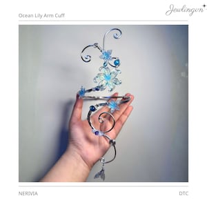 May include: An arm cuff featuring silver-toned wire shaped into swirling patterns, adorned with translucent blue lily-shaped flowers, small blue and white beads, and a small silver-toned mermaid tail charm hanging from the bottom wire end.