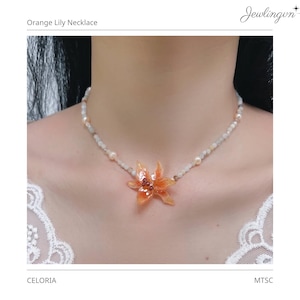 Può includere: Una collana con un ciondolo centrale a forma di giglio arancione con accenti rosso scuro, infilato su una catenina delicata composta da piccole perle pallide e traslucide e perle bianche rotonde. Il testo "Orange Lily Necklace" è visibile in alto.