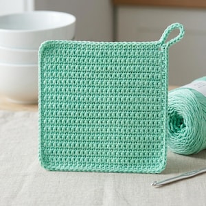 May include: A square, mint green crochet potholder with a loop for hanging. The potholder is made of a tightly woven stitch and is displayed on a neutral surface. A ball of matching yarn and a crochet hook are visible.