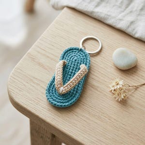 Può includere: Un portachiavi a forma di infradito turchese all'uncinetto, con cinturini beige e un anello argentato. L'accessorio fatto a mano è una versione in miniatura di un sandalo, perfetto per gli amanti della spiaggia. Misura circa 7.6 cm di lunghezza.