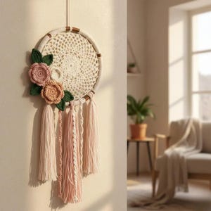 May include: A handcrafted dreamcatcher with a cream-colored crocheted web and a wooden hoop. It features pink and peach-colored crocheted flowers with green leaves, and cream and pink tassels hanging below. A decorative wall hanging.