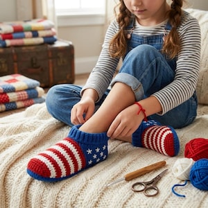 May include: A pair of handmade crochet slippers in red, white, and blue, resembling the American flag. The slippers feature red and white stripes, blue cuffs, and white stars. Crochet hooks, scissors, and yarn balls are also visible.