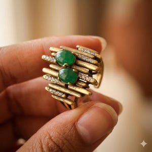 May include: A gold-toned ring featuring a textured, layered bar design with two oval-shaped green cabochon stones stacked vertically in the center and small, clear, round-cut stones embedded along the metallic bars for added detail.