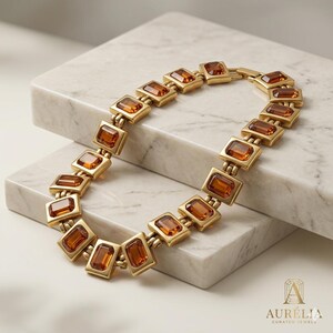 May include: A gold-toned link bracelet featuring a series of rectangular amber-colored gemstones set in metal frames. The bracelet is arranged in a curved shape and includes a clasp mechanism. The text Aur&eacute;lia Curated Jewels is visible.
