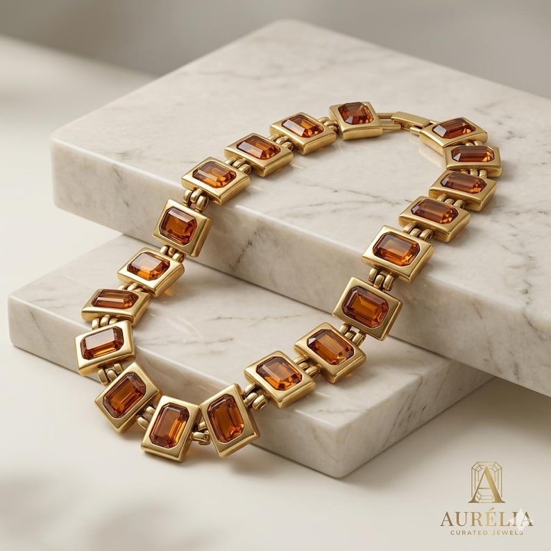 May include: A gold-toned link bracelet featuring a series of rectangular amber-colored gemstones set in metal frames. The bracelet is arranged in a curved shape and includes a clasp mechanism. The text Aur&eacute;lia Curated Jewels is visible.