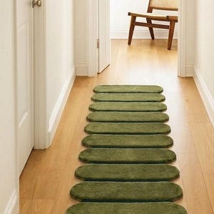May include: A long runner rug composed of eleven individual, olive green, oval-shaped segments arranged in a straight line. Each segment features a soft, textured pile surface with rounded edges, creating a continuous path-like appearance on the floor.