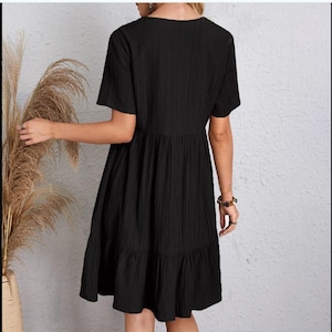 Puede incluir: Vestido negro de manga corta con un patrón texturizado de rayas verticales. El vestido presenta un escote en V, un corpiño ajustado y una falda acampanada con un dobladillo con volantes. El vestido llega a la rodilla.