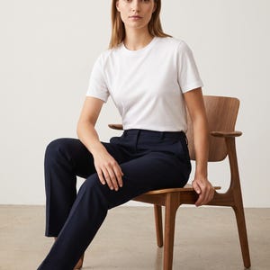 May include: A plain white short-sleeved crew neck t-shirt paired with solid navy blue trousers. The t-shirt features a simple round neckline and standard fit, while the trousers have a straight-leg cut with a clean, tailored appearance.