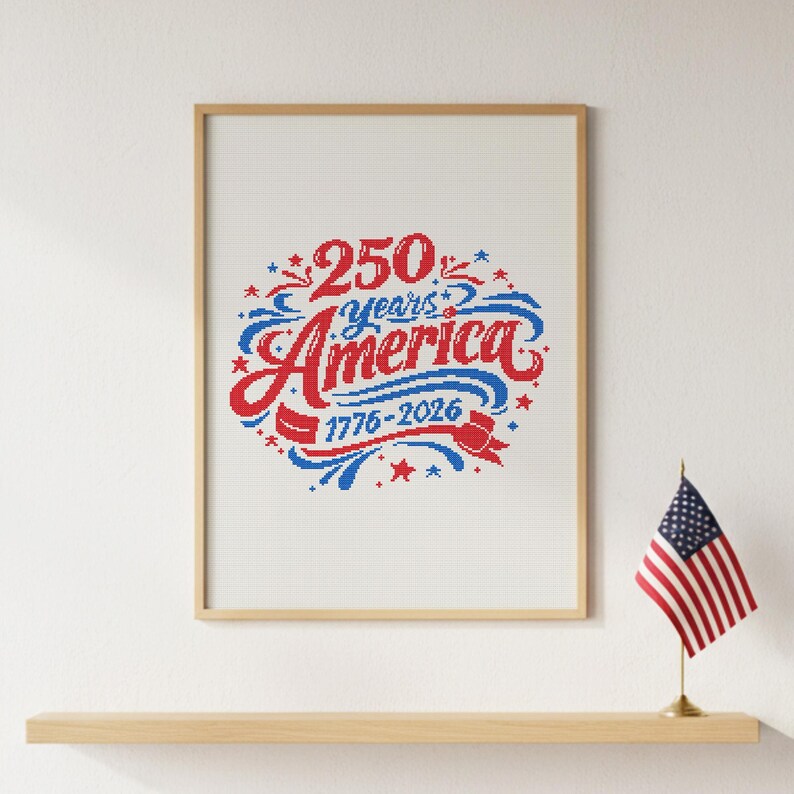 May include: A framed print with the words "250 Years America 1776-2026" in red and blue script. The print is in a wooden frame and sits on a shelf with a small American flag.