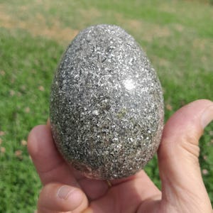 May include: An egg-shaped object with a smooth, glossy surface filled with dense, reflective silver and metallic grey flecks. The object has a rounded top and a slightly wider base, creating a solid, uniform, and highly textured appearance.