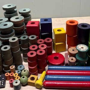 May include: A collection of colorful wooden toys, including blocks, spools, cylinders, and rods. The toys are in various shapes and sizes, with colors like red, blue, green, yellow, and orange. Some blocks have printed designs.
