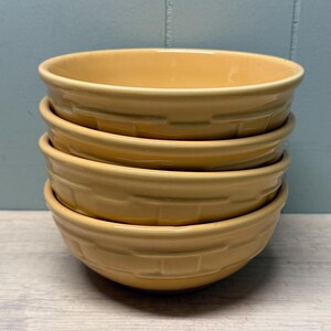 Peut inclure: Une pile de quatre bols en céramique jaune assortis. Chaque bol présente un motif en relief tressé façon panier sur le côté extérieur. Les bols ont une finition lisse et brillante ainsi qu'une forme arrondie avec une couleur jaune uniforme.