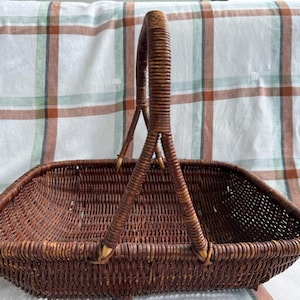 May include: A rectangular dark brown woven basket featuring a single tall arched handle. The basket is constructed with a tight, uniform weave pattern throughout the base and sides, with the handle securely attached at the center of each side.