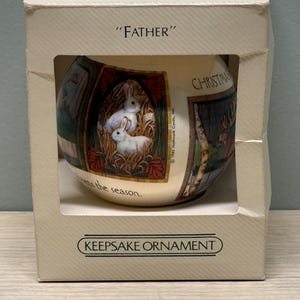 May include: A boxed Hallmark Keepsake Christmas ornament. The spherical ornament features painted scenes of rabbits and deer. The box is labelled "FATHER" and "KEEPSAKE ORNAMENT".