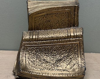 Könnte beinhalten: Eine dekorative Skulptur in Form von zwei gestapelten Büchern mit metallisch goldener Oberfläche. Die Oberfläche weist eine texturierte, rissige Optik mit sichtbaren Buchrücken und Seitenkanten auf. Das Objekt ist massiv und wirkt antik.
